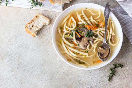 Vegan noodles soup with mushrooms and vegetables served with thyme, light concrete background. Selective focus. Top view.の写真素材
