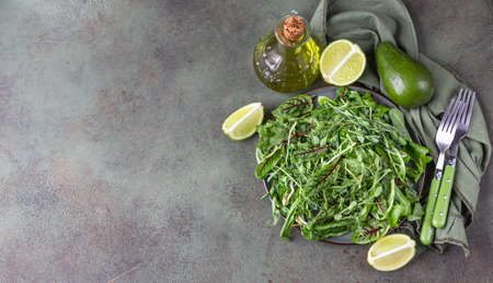 Plate with green mix salad leaves and microgreens, lime, avocado and olive oil on green concrete background. Vegan or vegetarian healthy food concept. Selective focus. Top view. Copy space.の写真素材