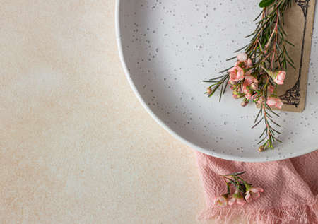 Romantic, wedding or spring table setting. Empty plate with card and little pink flowers, light concrete background. Flat lay. Selective focus.の写真素材