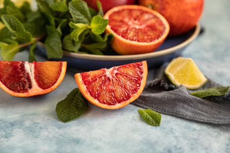 Red Sicilian oranges with limes and mint on blue background. Whole and sliced citrus. Selective focus.の写真素材