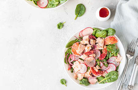 Fresh salad with salmon, spinach, radish and red oranges served with orange sauce on light concreteの写真素材