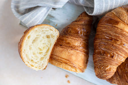 Cut in half croissant with inside texture and thin crisp layers on wooden board on light concreteの写真素材