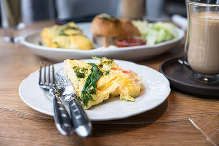 Omelette with spinach and tomatoes served with toasts, salad leaves and tomato sauce on a plate on wooden table. Healthy breakfast or brunch in cafe. Sunny morning. Selective focus.の写真素材