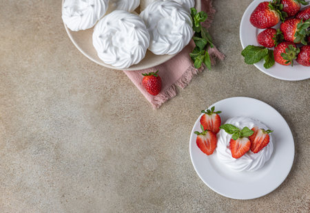 Mini meringue nest with fresh strawberries and mint on a plate, empty meringue nest and strawberries on concrete background. Selective focus. Top view. Copy space.の写真素材