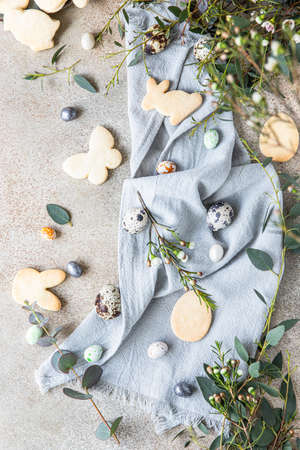 Easter cookies with candies shaped eggs, floral decor and quail eggs on linen napkin, stone...