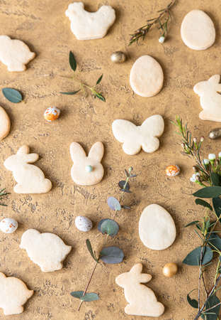 Easter cookies with candies shaped eggs, eucalyptus and flowers, stone background. Butter and sugar...