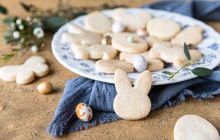 Easter cookies on a ceramic plate with floral decor and candies shaped eggs, stone background....