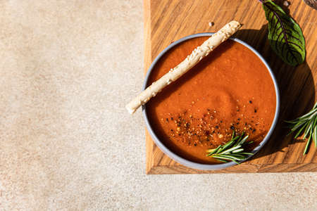 Fresh tomato gazpacho with ground pepper, greens and grissini or bread sticks. Direct sunlight and hard shadows. Selective focus. Top view.の写真素材