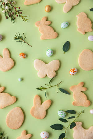 Easter cookies, candies shaped eggs, eucalyptus, flowers and quail eggs on green pastel background. Happy Easter concept. Pattern. Selective focus. Top view.の写真素材