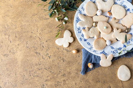 Easter cookies on a ceramic plate with floral decor and candies shaped eggs. Homemade butter and...