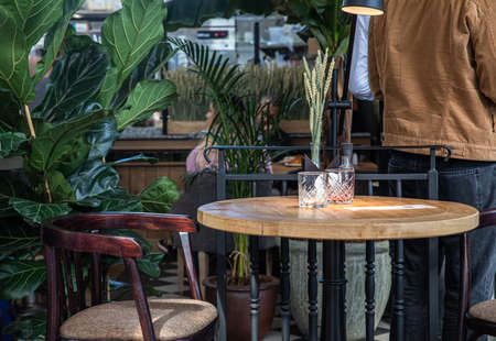 Details of the interior of modern cafe or coffee house with tropical plants, wooden tables, chairs...