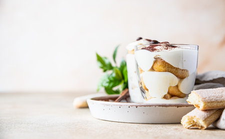 Traditional Italian dessert tiramisu in glass, light stone background. Coffee flavored portion dessert made of ladyfingers and mascarpone decorated with cocoa powder.の写真素材