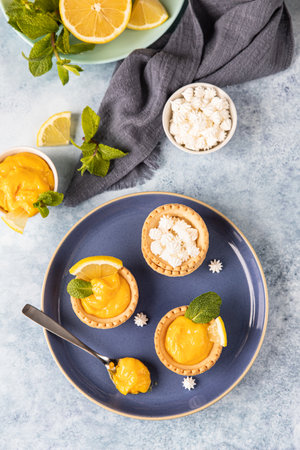 Mini tarts with lemon curd, mini meringue, lemon slices and mint on blue concrete background. Top view. Selective focus.の写真素材
