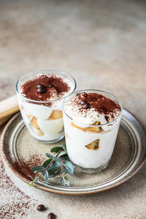 Traditional Italian dessert tiramisu in glass, light stone background. Coffee flavored portion dessert made of ladyfingers and mascarpone decorated with cocoa powder.の写真素材