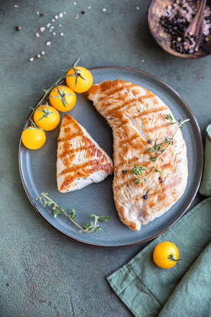 Grilled chicken or turkey breast with cherry tomatoes and thyme on a ceramic plate over green stone background.の写真素材