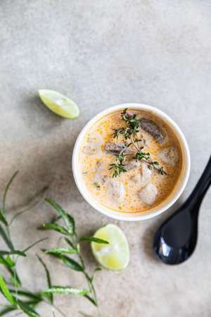 Traditional Asian soup Tom yum kung in disposable cup of craft paper. Soup to go, food delivery....
