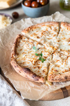 Homemade pizza with chicken and cheese on white sauce, light concrete background.