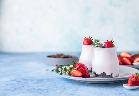 Healthy breakfast or dessert with natural yogurt, chocolate granola and strawberries, blue concrete background.の写真素材