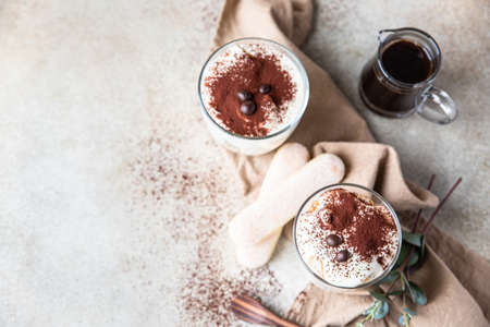 Traditional Italian dessert tiramisu in glass, light stone background. Coffee flavored portion...