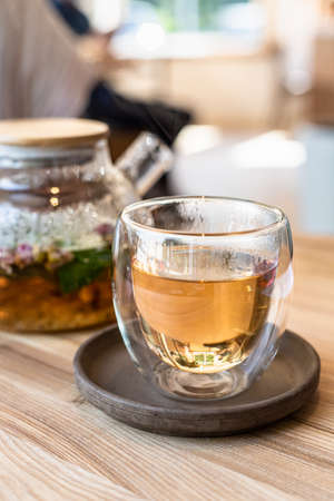 Glass cup with green or herbal tea and teapot on wooden table in cafe. Tea with mint and rose petals. Blurred background.の写真素材