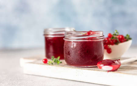 Homemade red currant jam or jelly in glass jars and red currants fresh berries on wooden cutting...