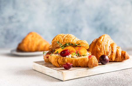 Croissant with nectarine, cherry and ricotta or cream cheese on wooden cutting board. Selective focus.の写真素材