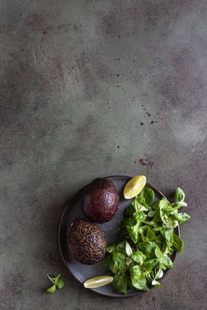 Avocado, green leaves salad and lime slices on green concrete background. Healthy fats. Selective...