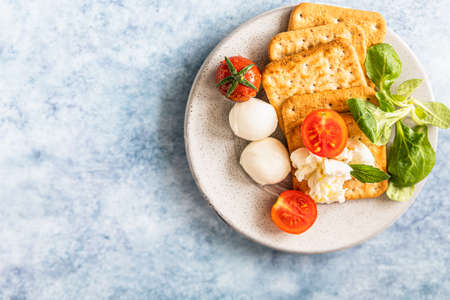 Crackers with cherry tomatoes, green salad and mozzarella, blue concrete background. Selective...