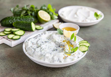 Traditional greek tzatziki dip sauce with grated cucumber, greek yogurt, olive oil and mint, green concrete background. Selective focus.の写真素材