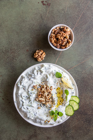 Traditional bulgarian cold summer soup tarator with ingredients on green background. Bulgarian soup with grated cucumbers, yogurt and walnuts. Selective focus. Top view.の写真素材