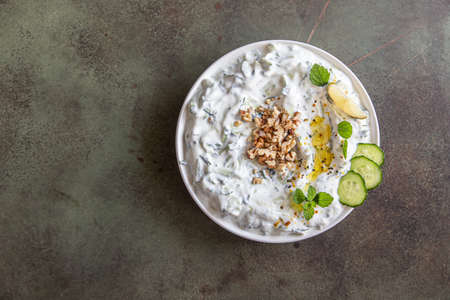 Traditional bulgarian cold summer soup tarator with ingredients on green background. Bulgarian soup with grated cucumbers, yogurt and walnuts. Selective focus. Top view.の写真素材