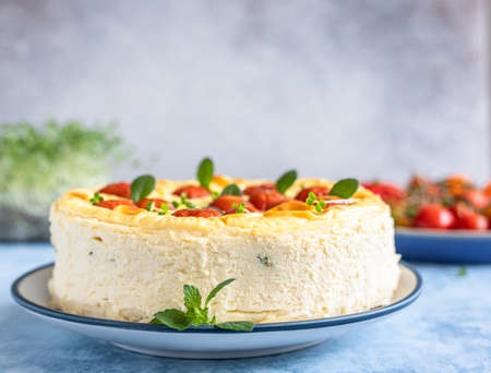 Savory cheesecake with tomatoes decorated with mint, blue concrete background. Selective focus.