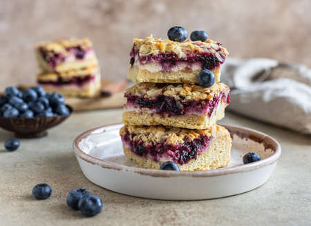 Crumble cheesecake bars with blueberry filling and fresh blueberries, concrete background. Bar...