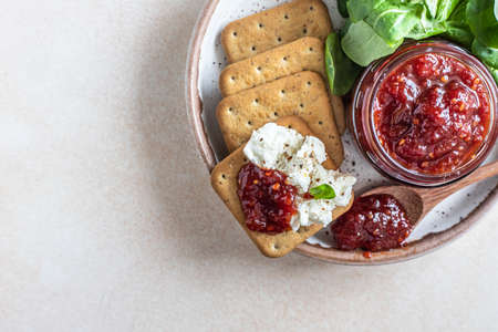 Tomato jam, confiture or sauce in glass jar with crackers and green leaves salad. Unusual savory jam. Mediterranean cuisine. Top view.の写真素材