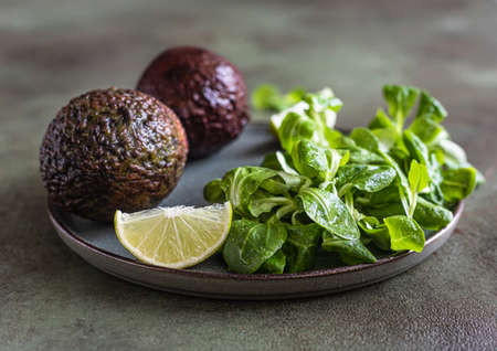 Avocado, green leaves salad and lime slices on green concrete background. Healthy fats.
