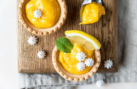 Lemon tartlets. Homemade shortbread mini tarts with lemon curd and meringue on wooden board, light concrete background. Top view.の写真素材