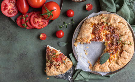 Savory tomato tart, open pie or galette with tomatoes and cheese decorated with aromatic herbs on...
