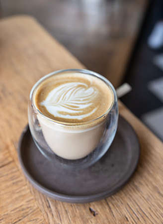 Coffee with latte art in cup on wooden table in cafe or coffee shop. Selective focus.の写真素材