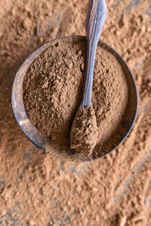 Carob powder in wooden bowl on dark concrete background. Substitute for cocoa. Healthy food concept....