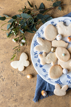 Easter cookies on a ceramic plate with floral decor and candies shaped eggs. Homemade butter and...