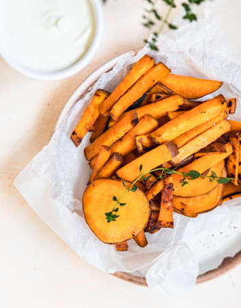 Healthy homemade baked sweet potato wedges with cream dip sauce and herbs on concrete background....