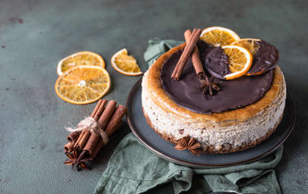 Cheesecake with chocolate decorated slices of dried oranges, cinnamon and anise on green stone background. Delicious homemade pastry. Selective focus.の写真素材