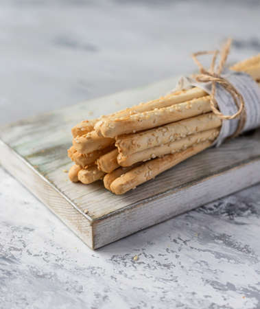 Italian grissini or salted breadsticks on a light stone background. Fresh italian snack with sesame...