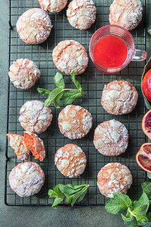 Delicious citrus crunchy orange crinkle cookies with powdered sugar on black metal grille, green concrete background.の写真素材