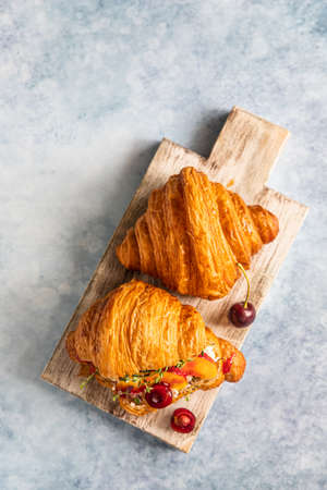 Croissant with nectarine, cherry and ricotta or cream cheese on wooden cutting board. Top view.の写真素材