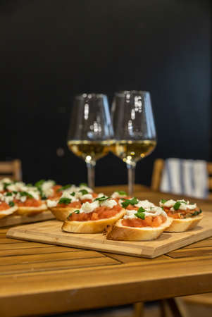Toast or bruschetta with tomatoes, mozzarella and basil and two glasses with white wine. An...