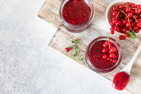 Homemade red currant jam or jelly in glass jars and red currants fresh berries on wooden cutting...