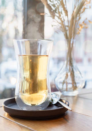 Glass cup with green or herbal tea on wooden table in cafe. Blurred window background.の写真素材