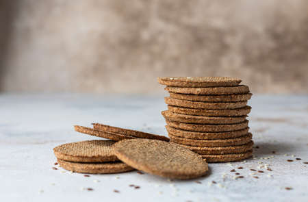 Stack of tasty crackers with sesame and flax seeds on gray background. Healthy snack. Selective...