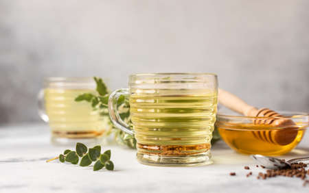Cup with buckwheat tea, granules and honey, light gray concrete background. Superfood Taiwan Ku Qiao buckwheat tea and grits of tartary buckwheat. Detox and healthy food.の写真素材